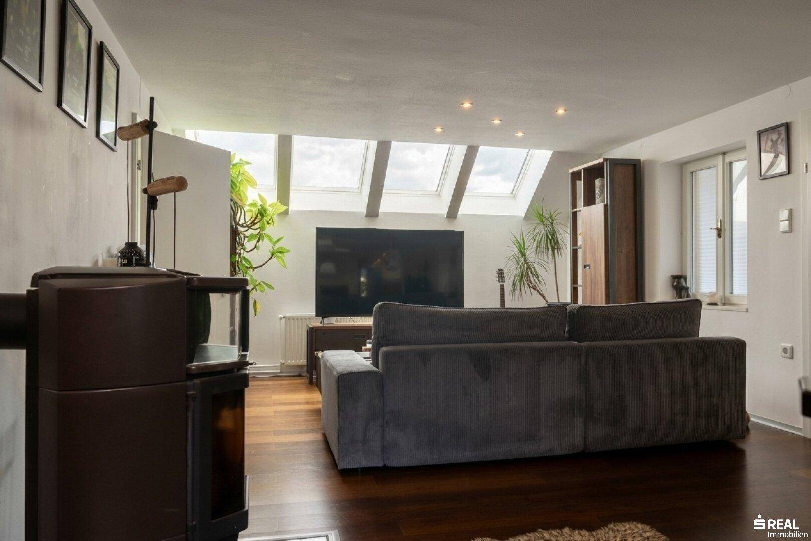 Geräumiges Wohnzimmer mit Holzboden, Dachschräge und mehreren Dachfenstern für viel Licht.