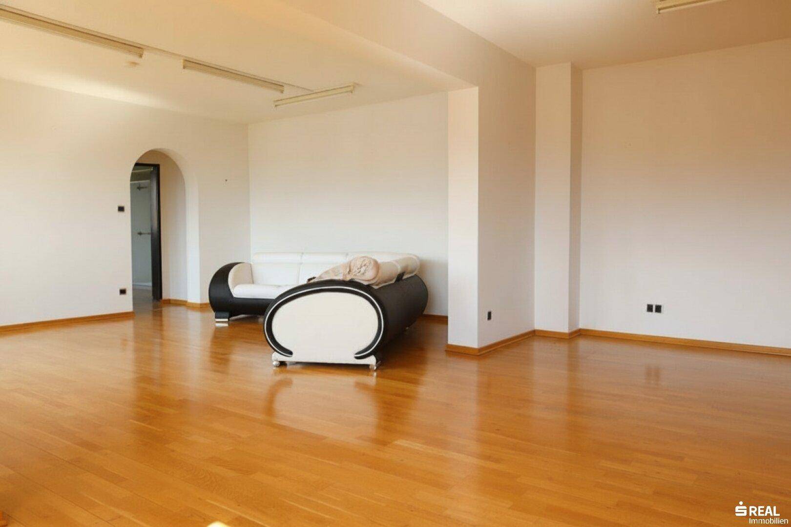 Geräumiges Wohnzimmer mit glänzendem Holzboden und minimalistischer Einrichtung.