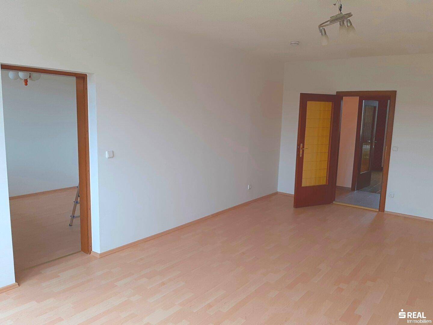 Geräumiges Wohnzimmer mit Laminatboden und Holztüren, bereit zur individuellen Gestaltung.