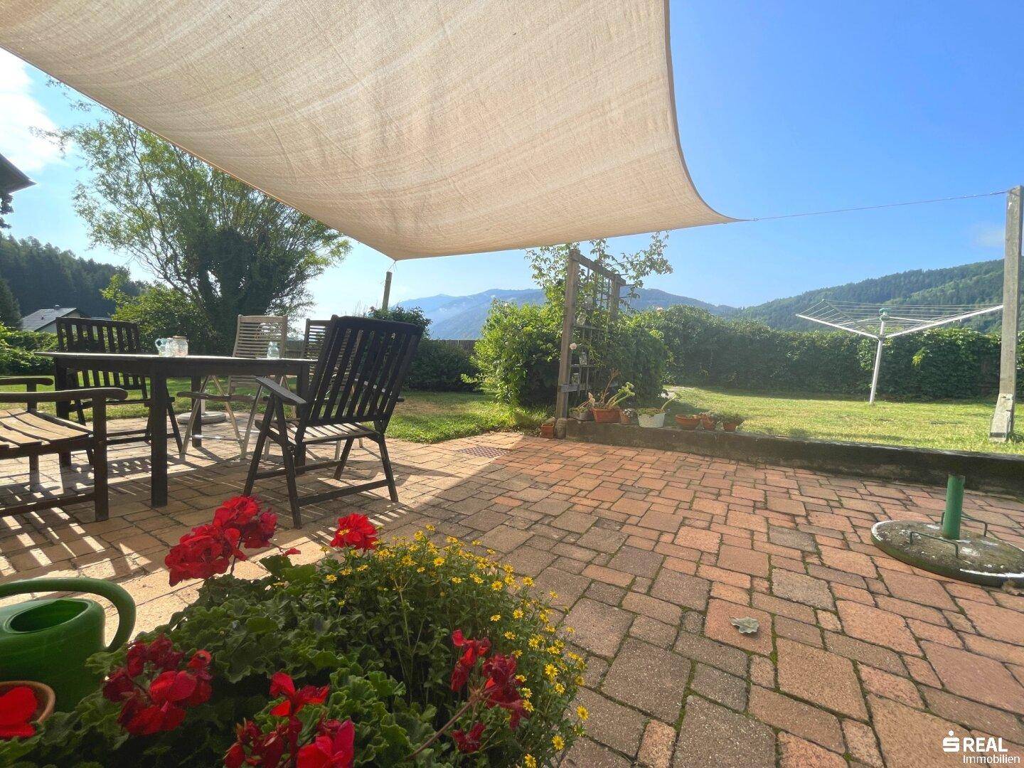 Sonniger Gartenbereich mit gepflasterter Terrasse, Sitzgelegenheiten und Wäscheleine im Hintergrund.