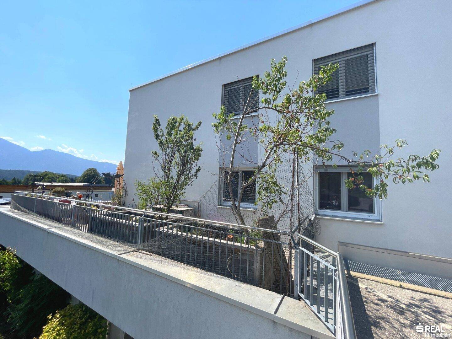 Moderne Gebäudefassade mit großen Fenstern und einer breiten Terrasse im oberen Stockwerk.