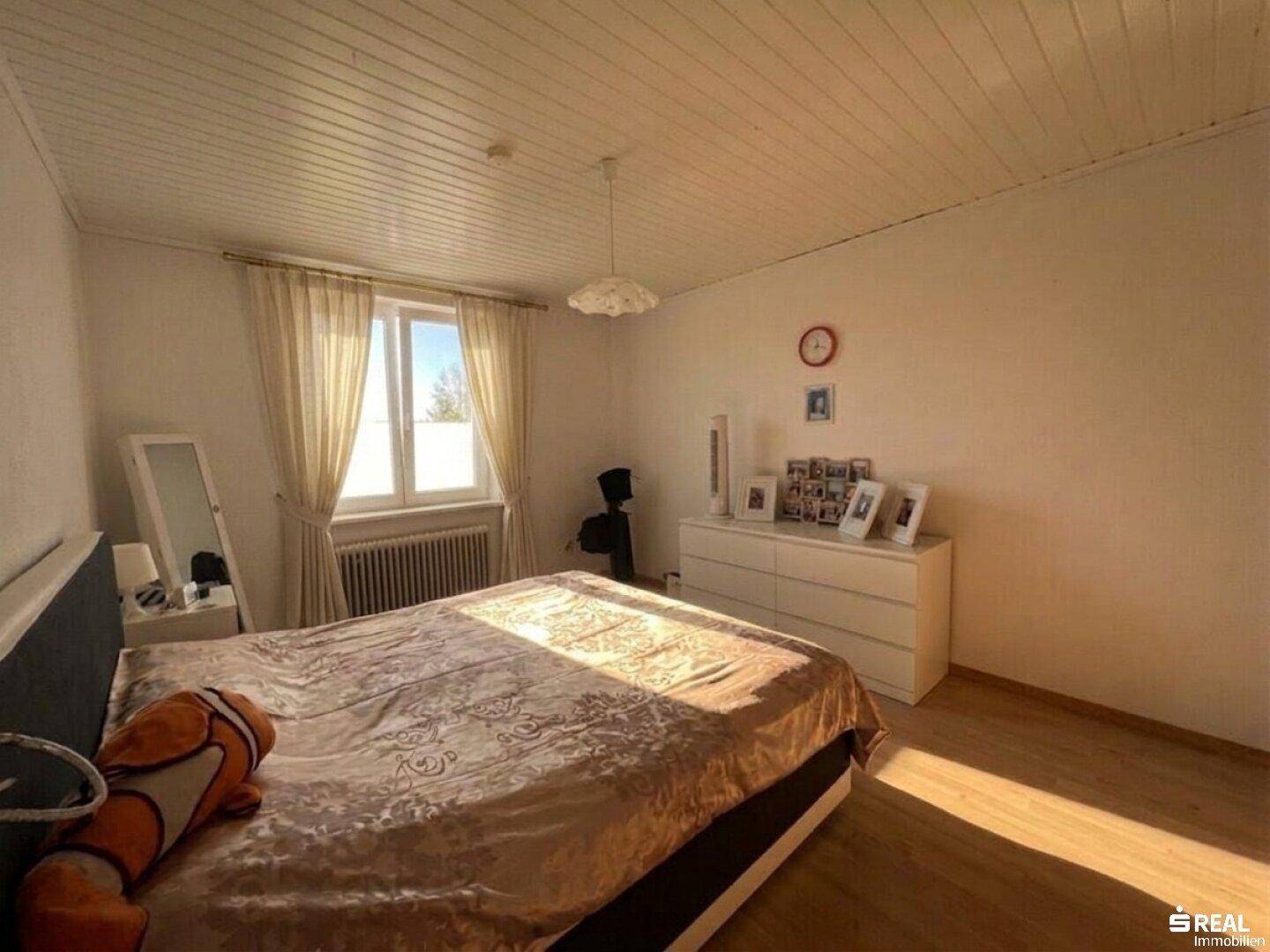 Geräumiges Schlafzimmer mit Doppelbett, Kommode, Holzboden und einer hellen Holzpaneeldecke.