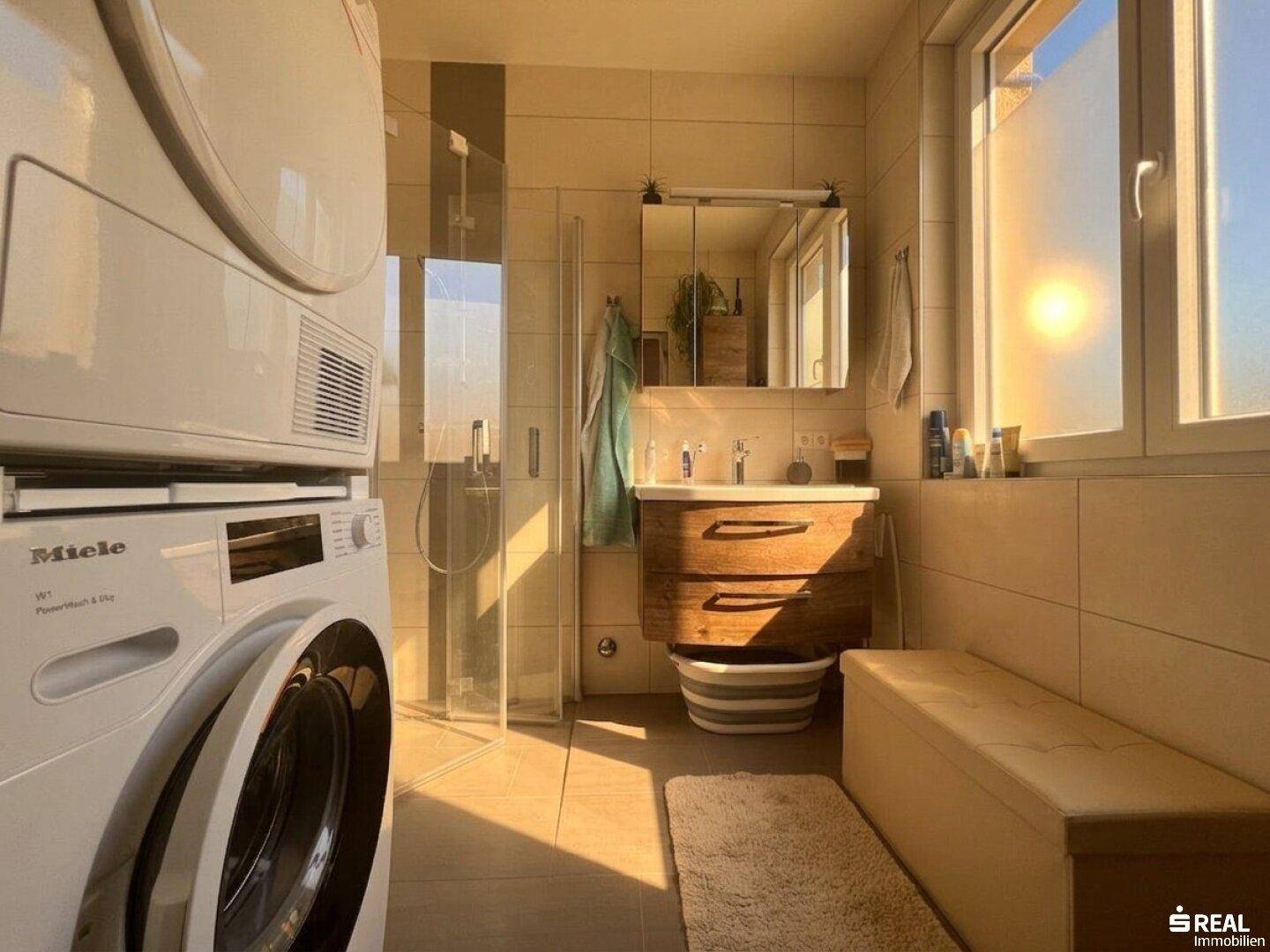 Modernes Badezimmer mit Dusche, Holzwaschtisch, Waschmaschine und Fenster für natürliches Licht.