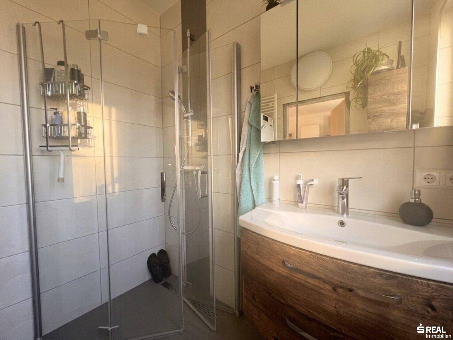 Detaillierte Ansicht des modernen Badezimmers mit Glasdusche und elegantem Holzwaschtisch.