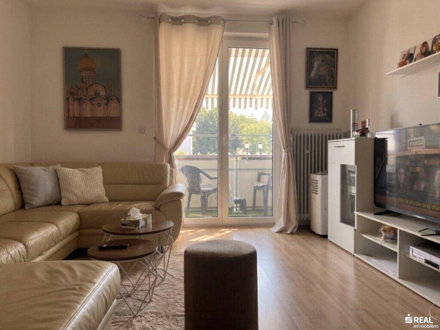 Gemütliches Wohnzimmer mit beigem Ecksofa, Holzboden und direktem Zugang zu einem Balkon.