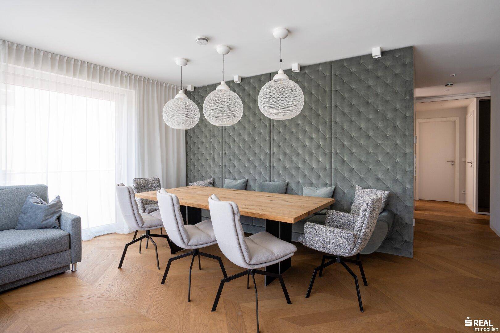 Eleganter Essbereich mit großem Holztisch, gepolsterter Sitzbank und modernen Pendelleuchten.