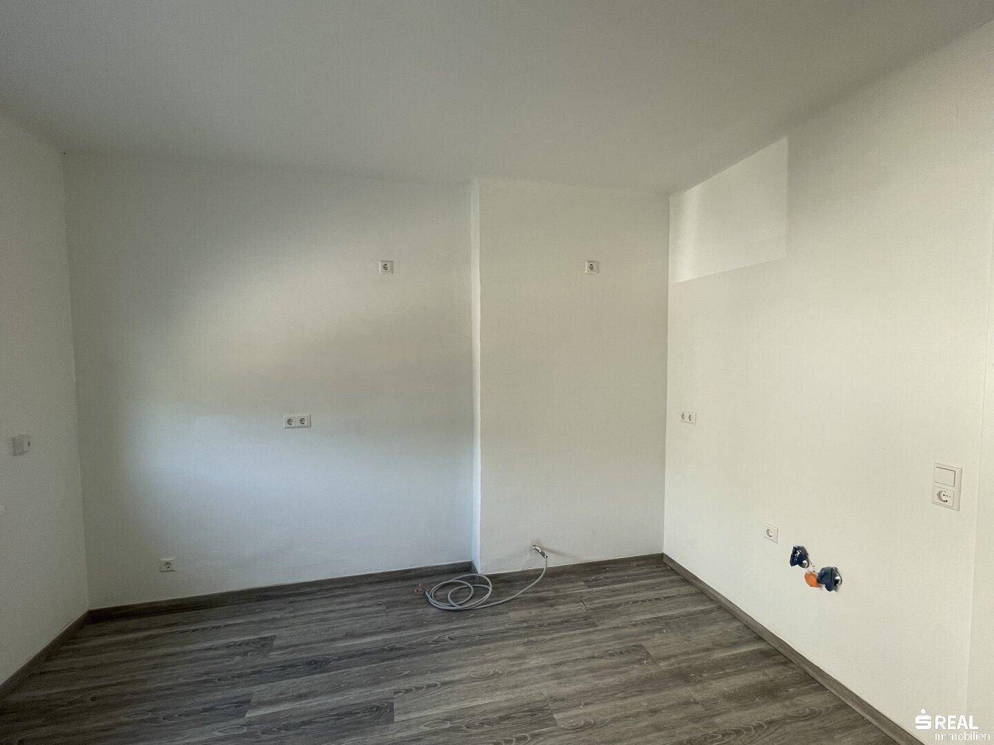 Leerer Raum mit Laminatboden und Anschlüssen an der Wand, bereit für die Einrichtung.