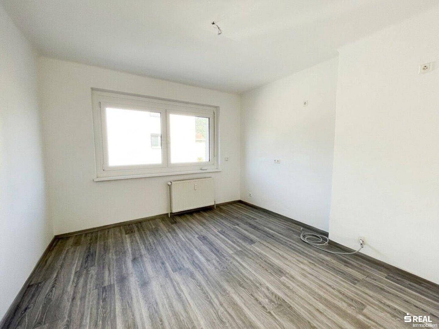 Unmöblierter Raum mit Laminatboden, Heizkörper und Fenster für Tageslicht.