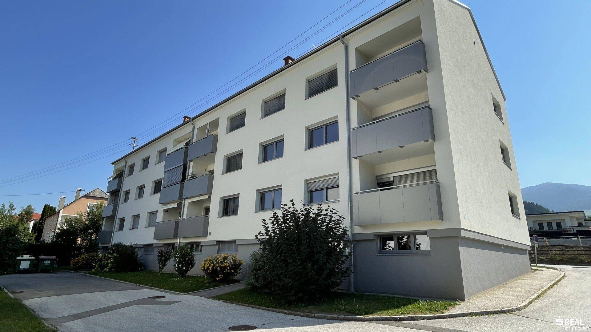 Modernes Mehrfamilienhaus mit Balkonen und gepflegter Außenanlage unter blauem Himmel.