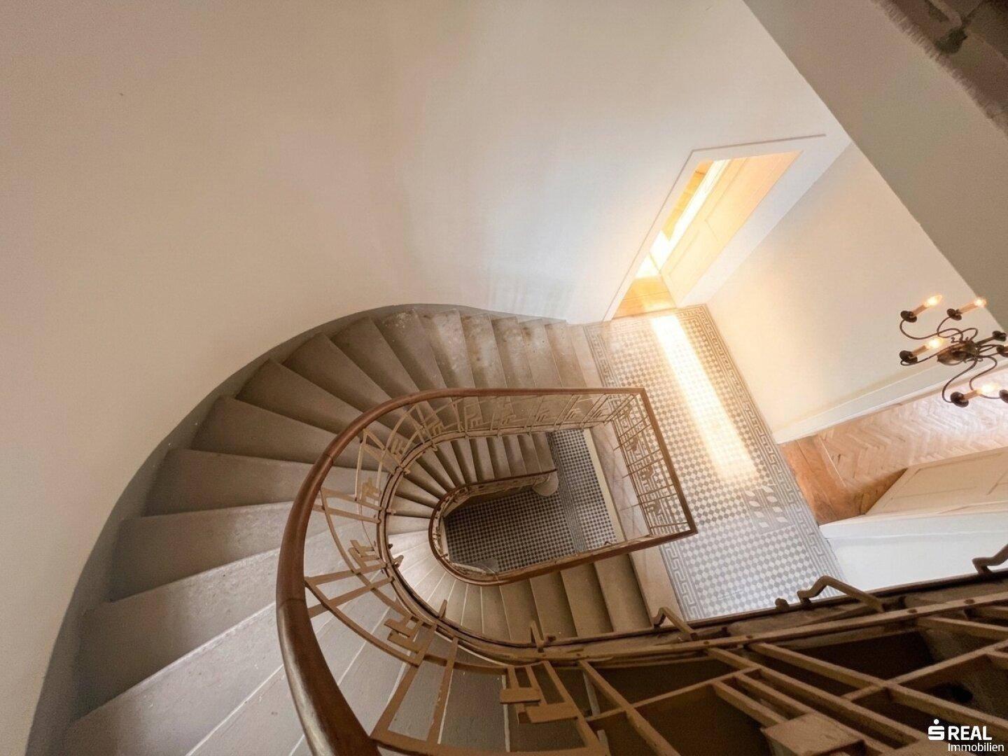 Elegante Wendeltreppe mit kunstvollem Geländer und gemusterten Fliesen im Eingangsbereich.