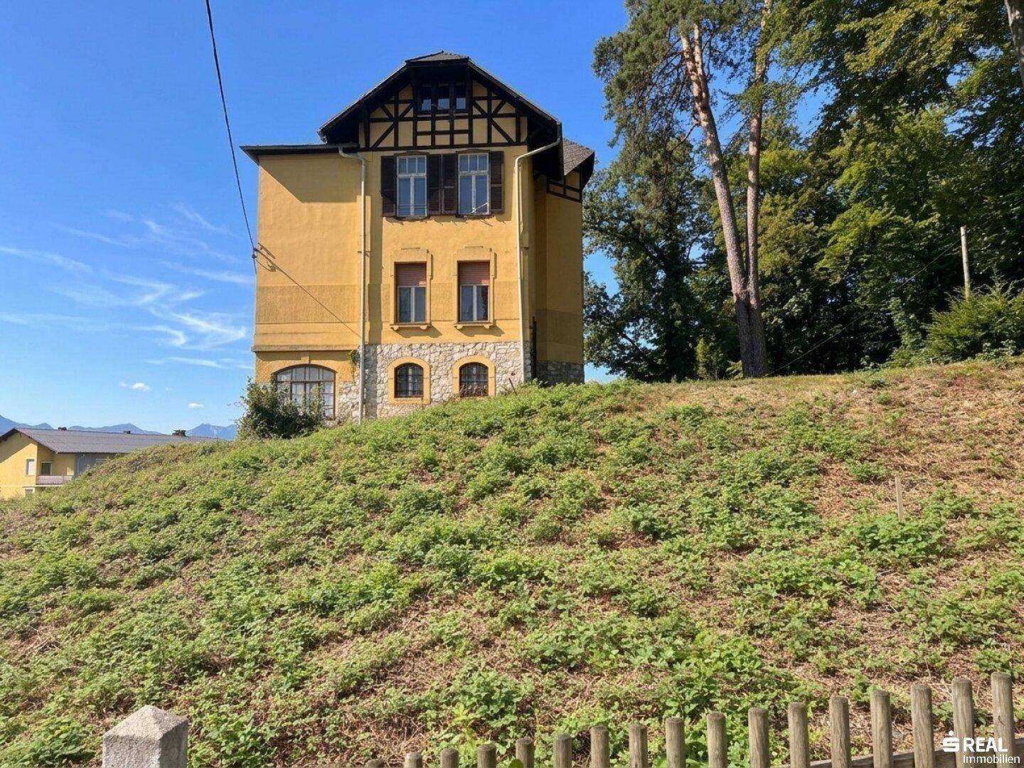 Die historische Villa auf einem grünen Hügel, umgeben von Natur und Bäumen.