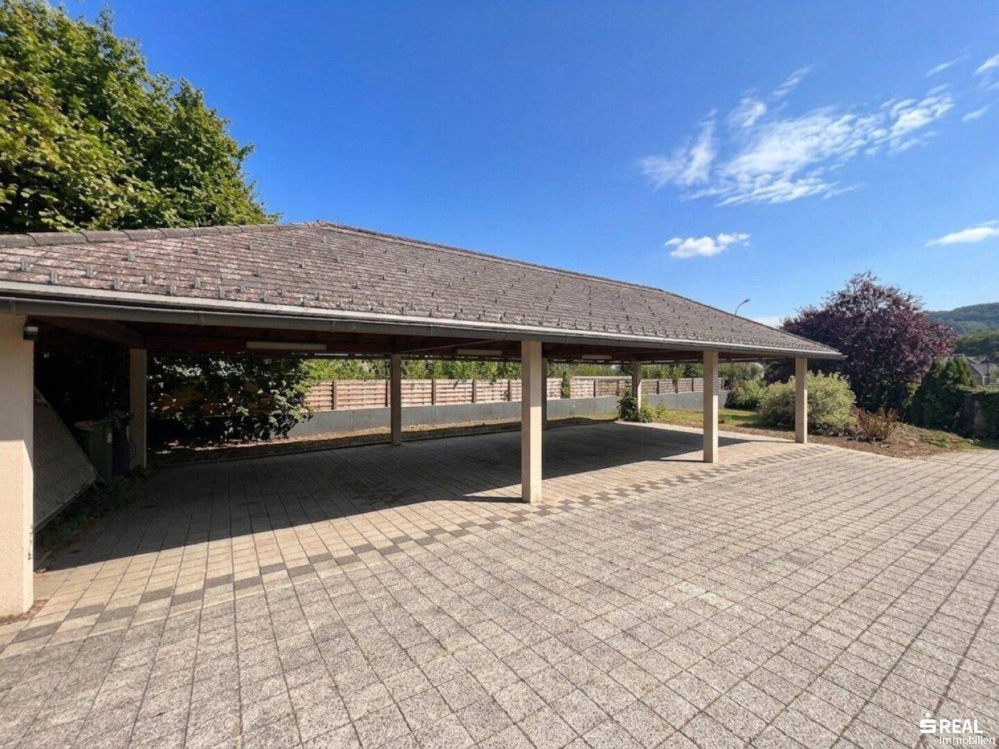 Geräumiger Carport mit mehreren Stellplätzen und gepflasterter Zufahrt, umgeben von Grün.