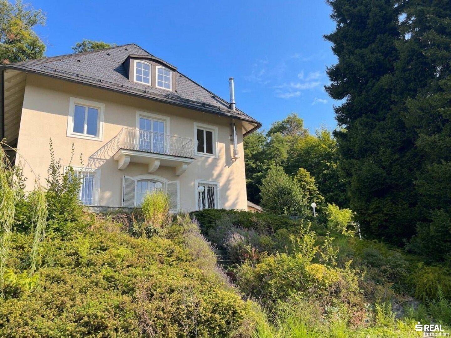 Seitenansicht der Villa mit kleinem Balkon und Fensterläden, umgeben von mediterraner Bepflanzung.