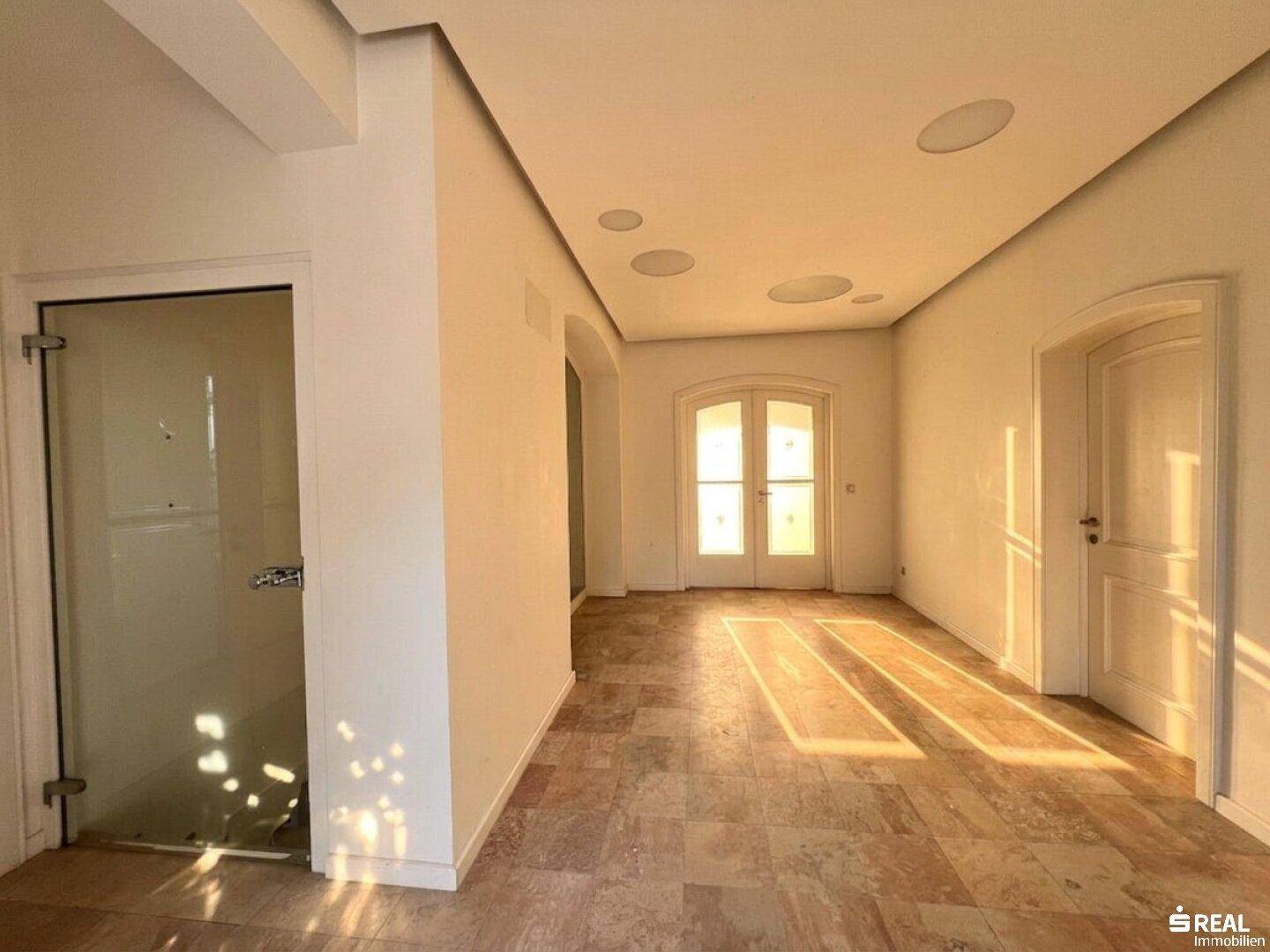 Heller Flur mit Steinboden und integrierten Deckenleuchten, führt zu weiteren Räumen.