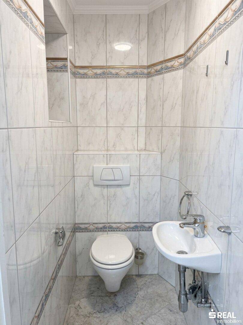 Kleines Gäste-WC mit Wand-WC und Waschbecken, ausgestattet mit hellen Fliesen.