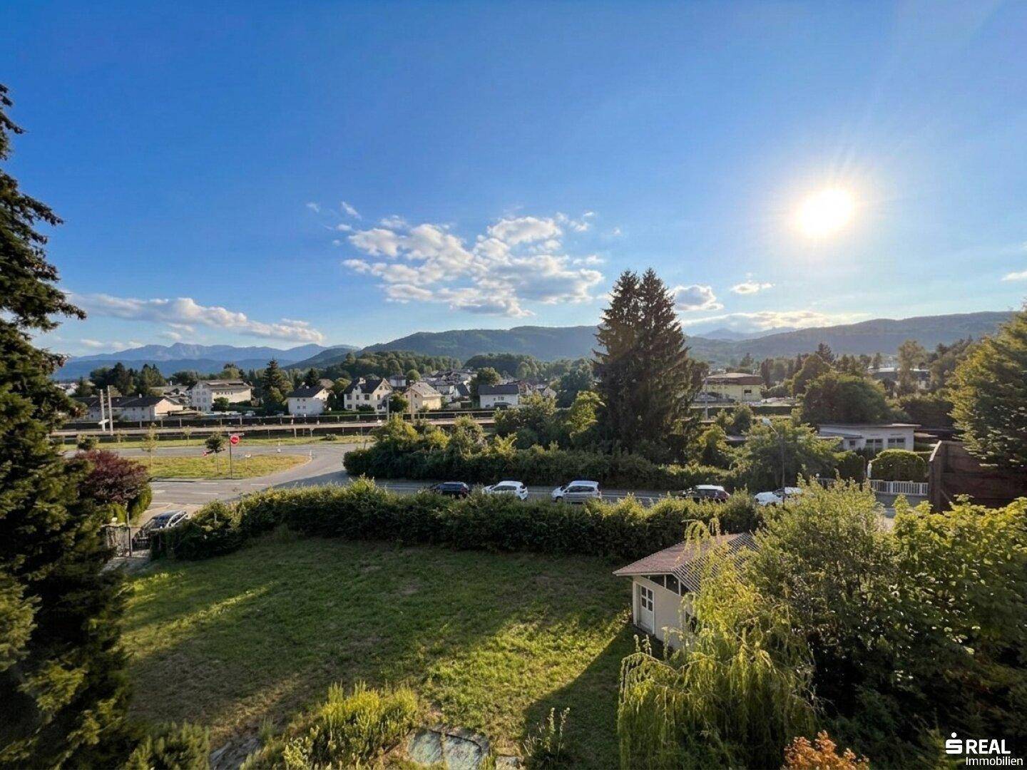 Weitläufiger Panoramablick über die Landschaft mit Bergen und Siedlung unter strahlendem Himmel.
