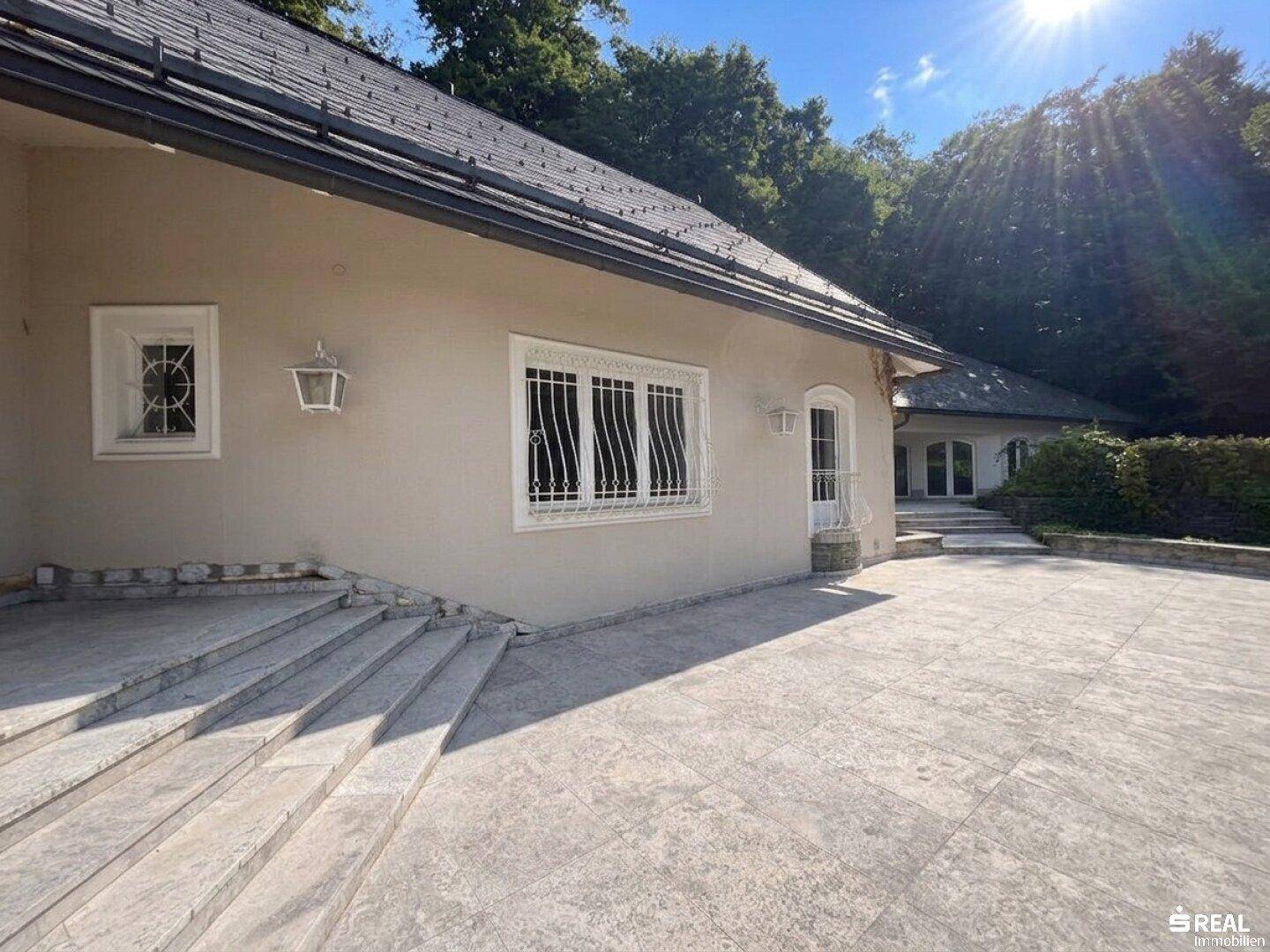 Seitenansicht der Villa mit großzügiger gepflasterter Fläche und Treppen.