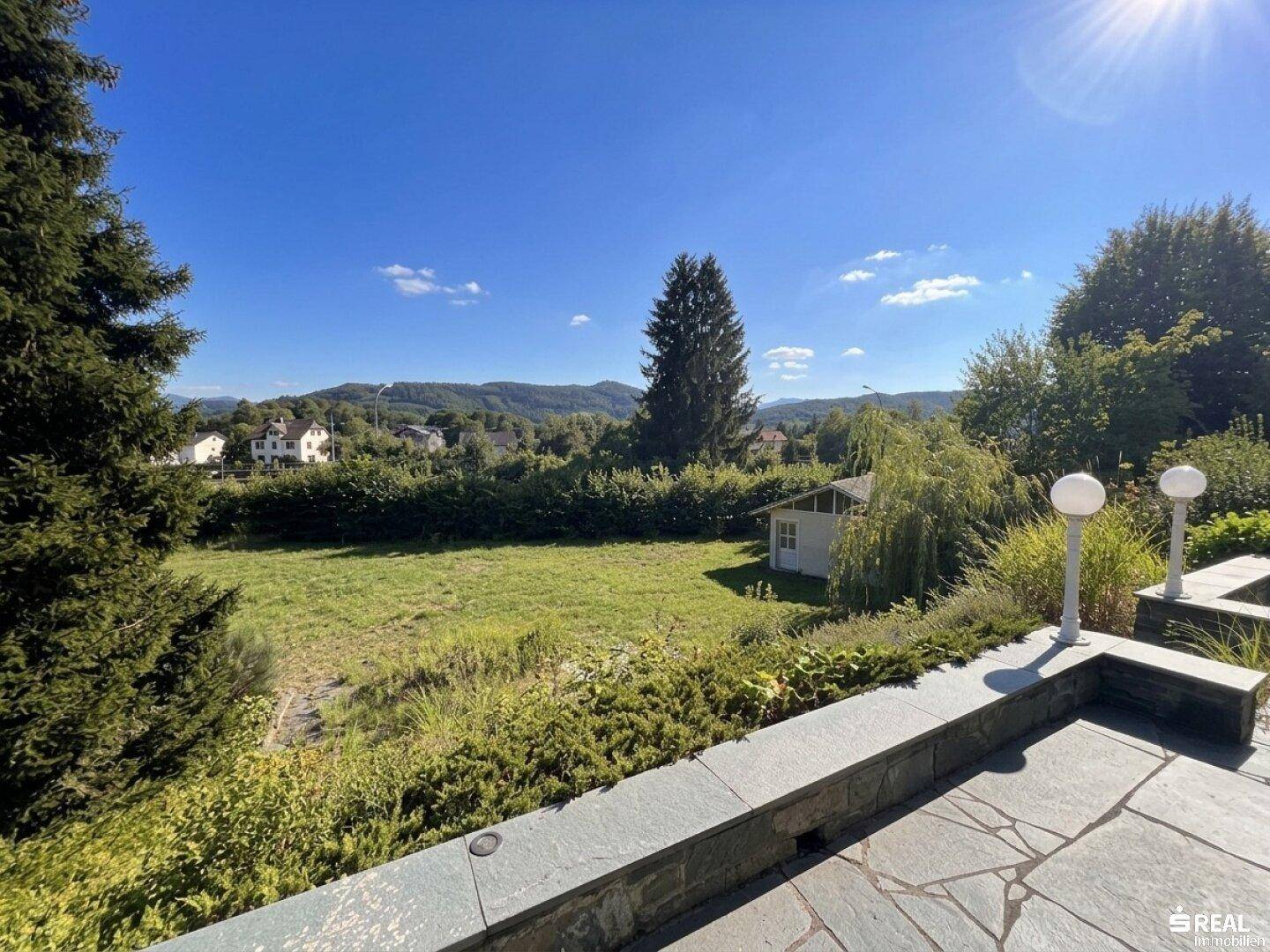 Weitläufiger Garten mit Rasenfläche, Gartenhaus und Panoramablick auf die Berge.