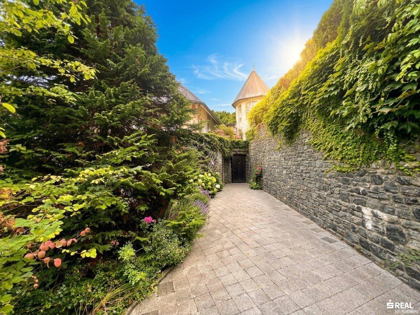 Malerischer Weg mit Steinmauer und üppiger Vegetation, der zum Eingang führt.
