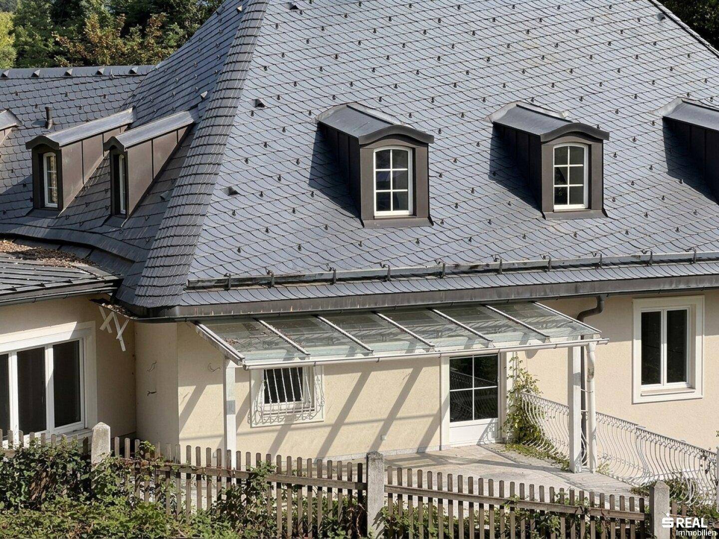 Detailansicht des Schieferdaches mit Gaubenfenstern und einem überdachten Eingangsbereich.