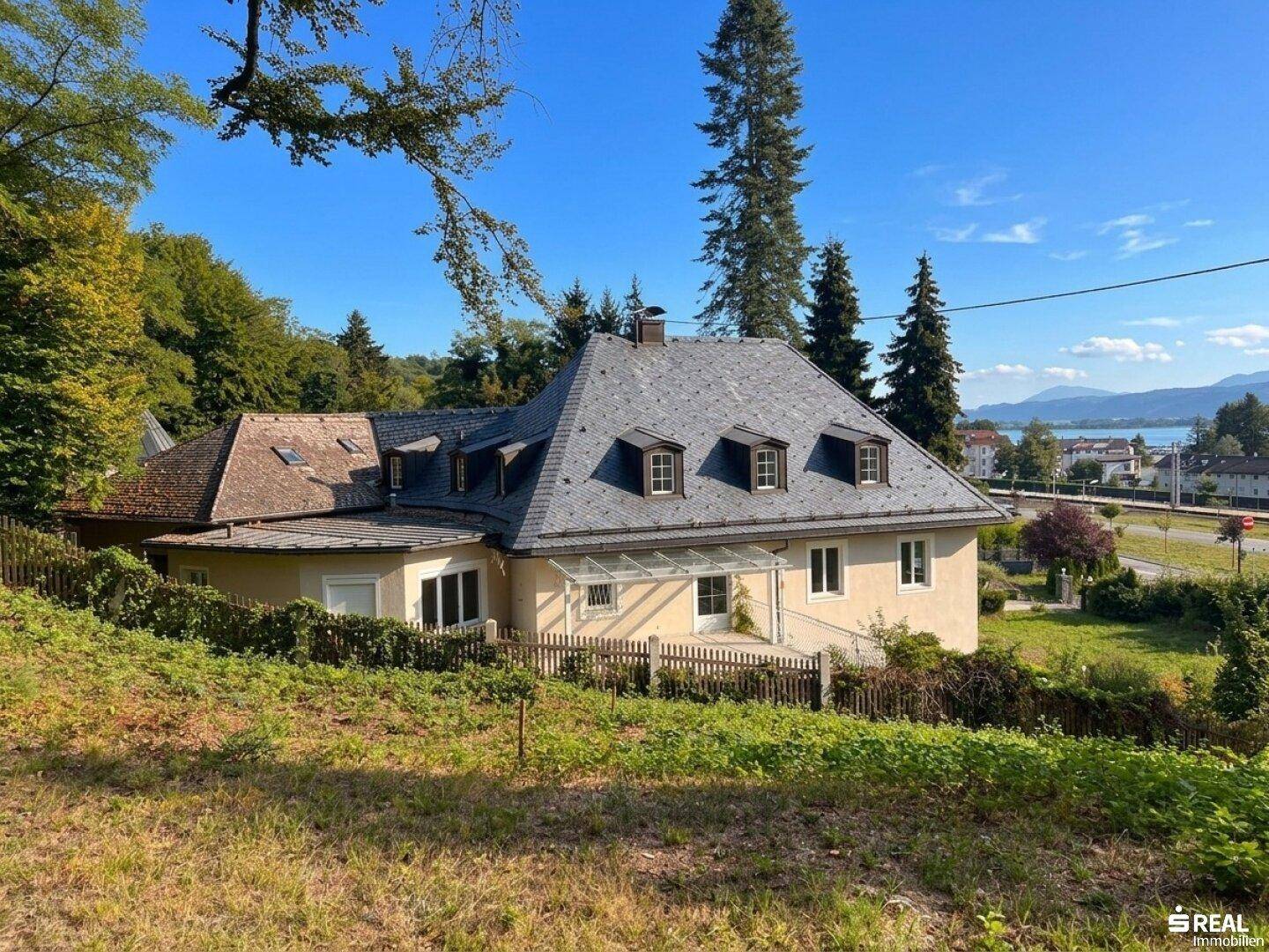 Malerische Villa mit Schieferdach und Seeblick, eingebettet in eine grüne Hügellandschaft.