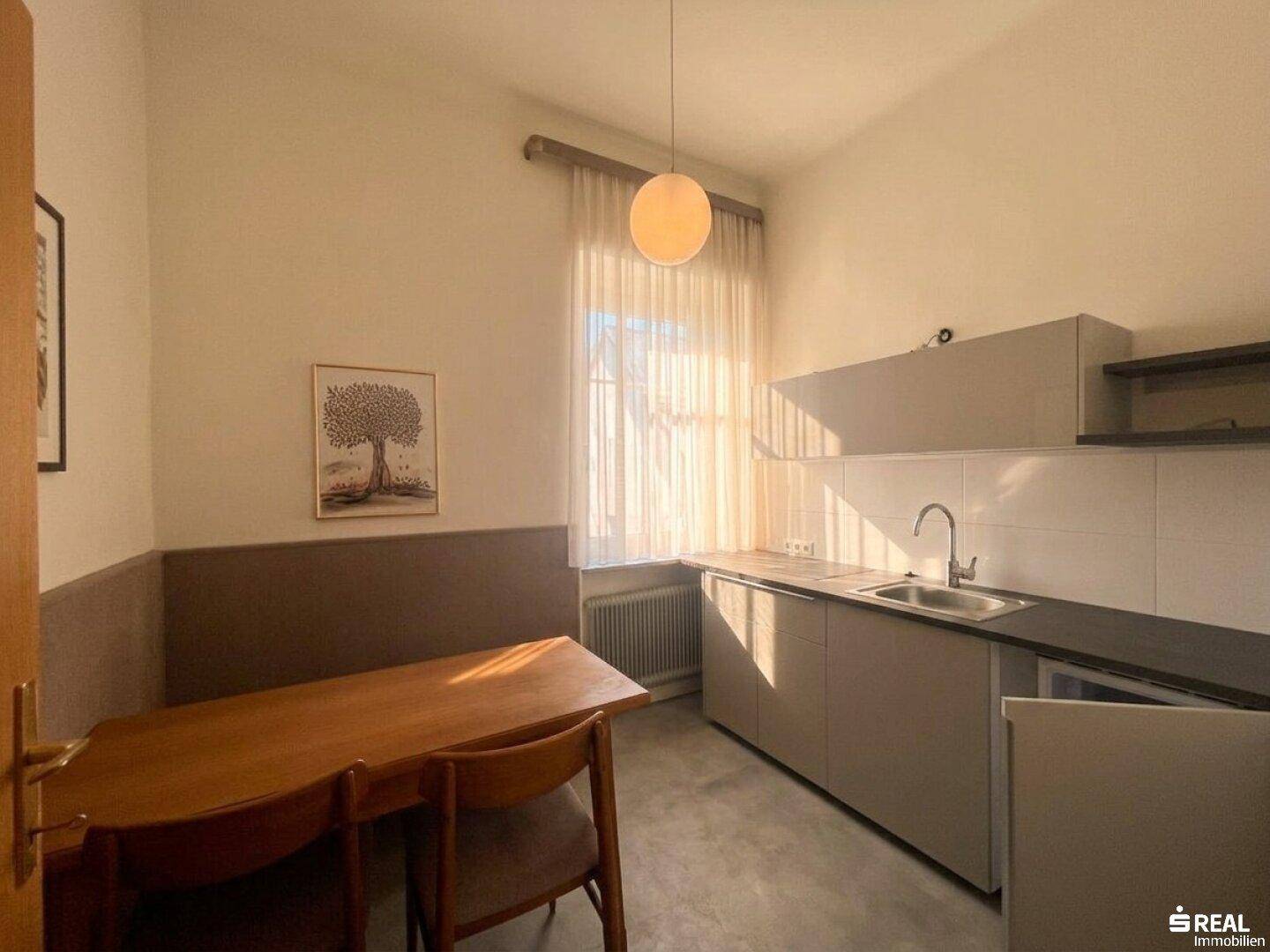 Kleine Küchenzeile mit integriertem Essbereich, ausgestattet mit Spüle und Unterschränken, ideal für kompaktes Wohnen.