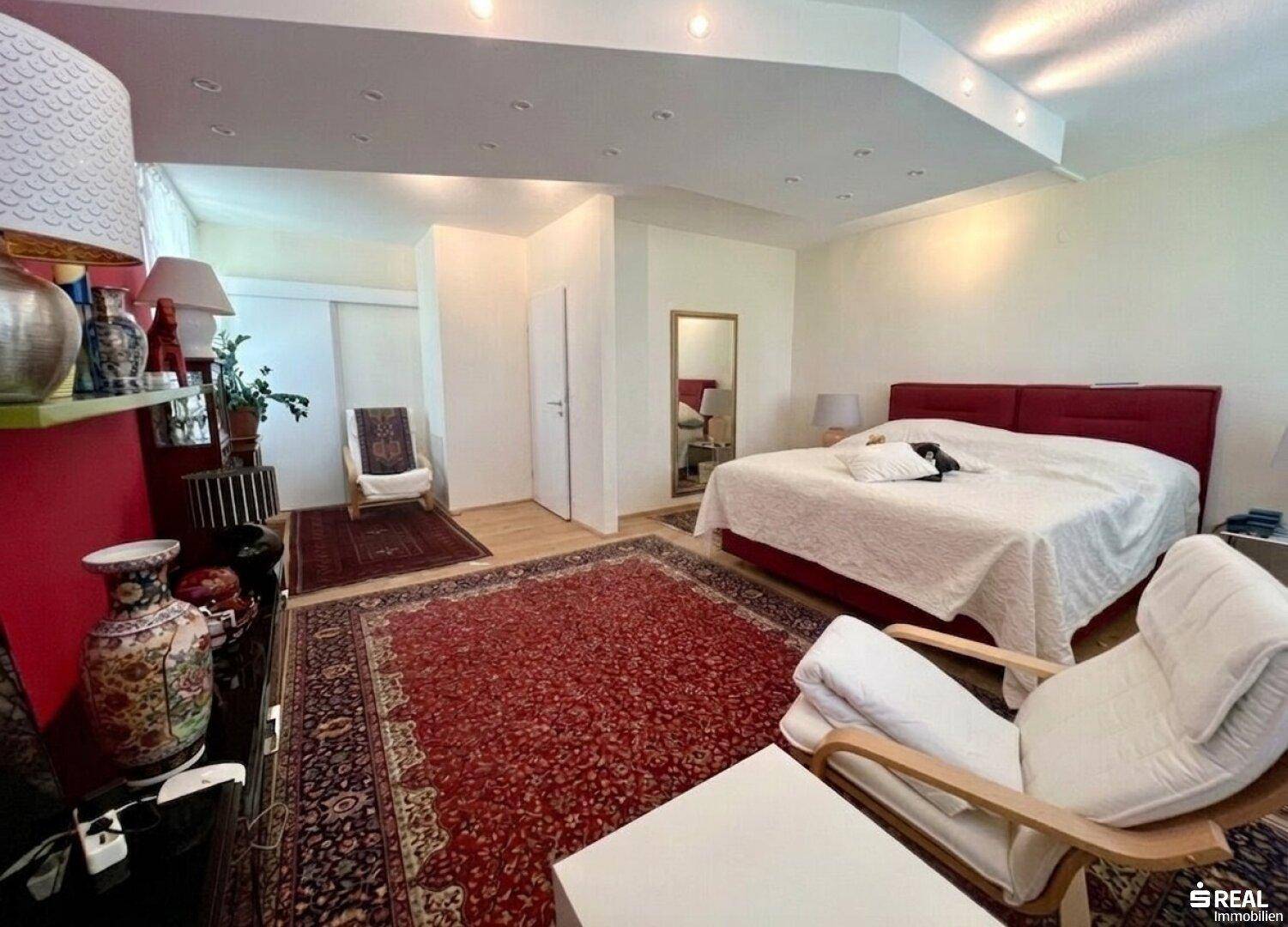 Geräumiges Schlafzimmer mit rotem Teppich, Holzboden und indirekter Deckenbeleuchtung.
