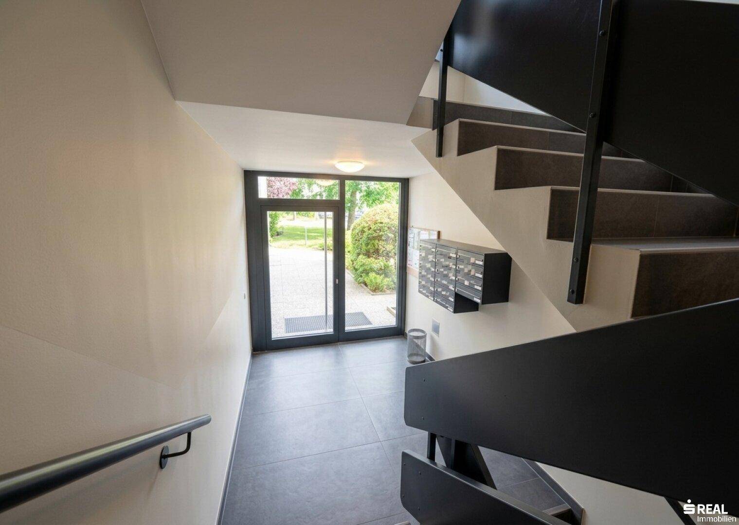 Treppenhaus im Mehrfamilienhaus mit dunklen Stufen und modernem Geländer.