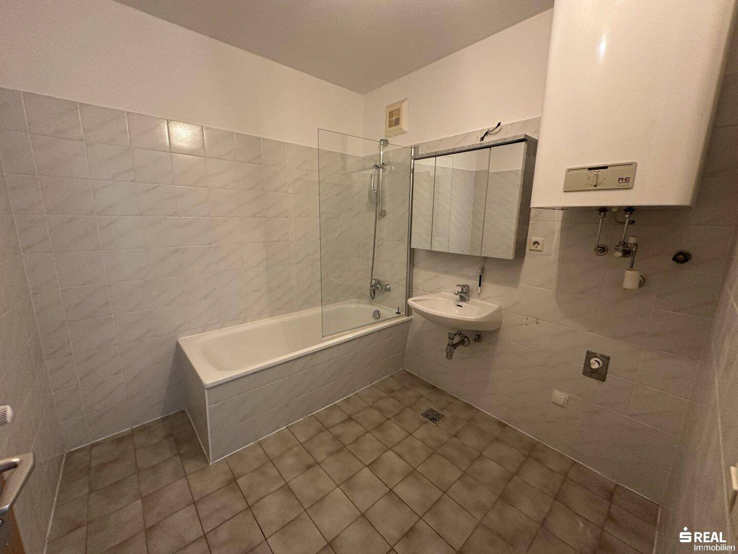 Badezimmer mit Fliesen, Badewanne mit Duschwand, Waschbecken und Spiegelschrank.