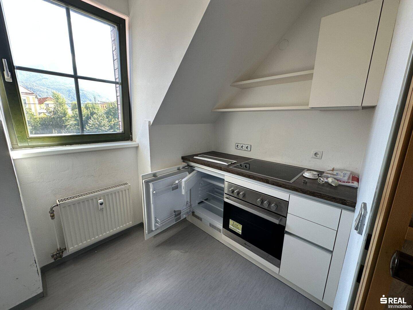 Kleine Küche mit Einbaugeräten, Kochfeld, Backofen und Kühlschrank unter der Dachschräge.
