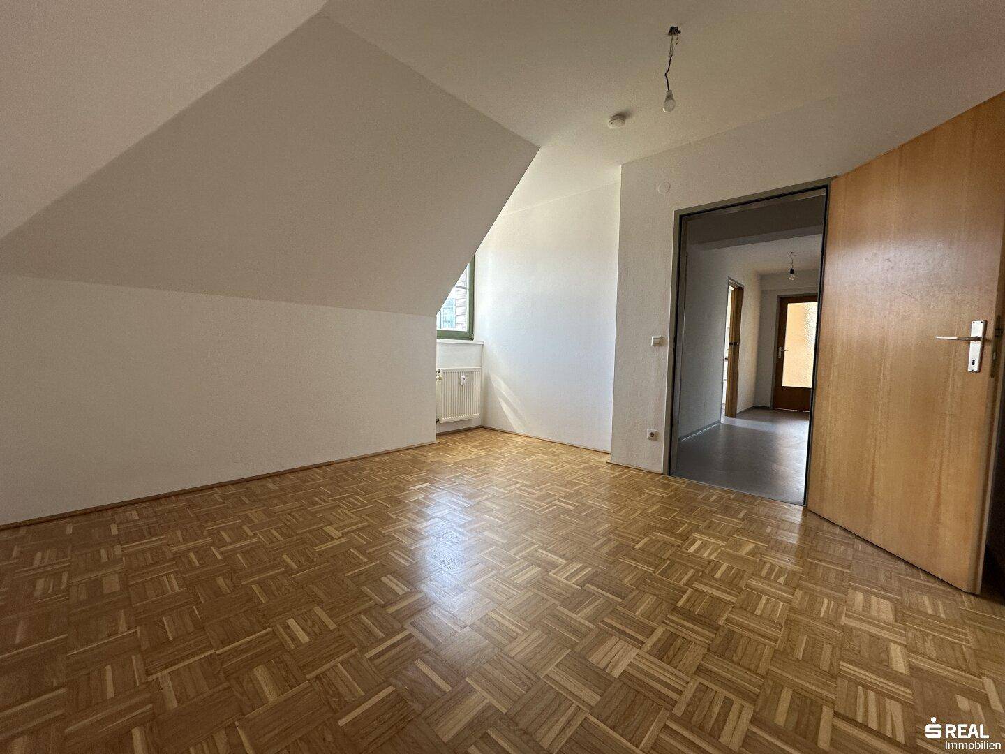 Geräumiges Zimmer mit Parkettboden, Dachschräge und Zugang zu einem Flur.