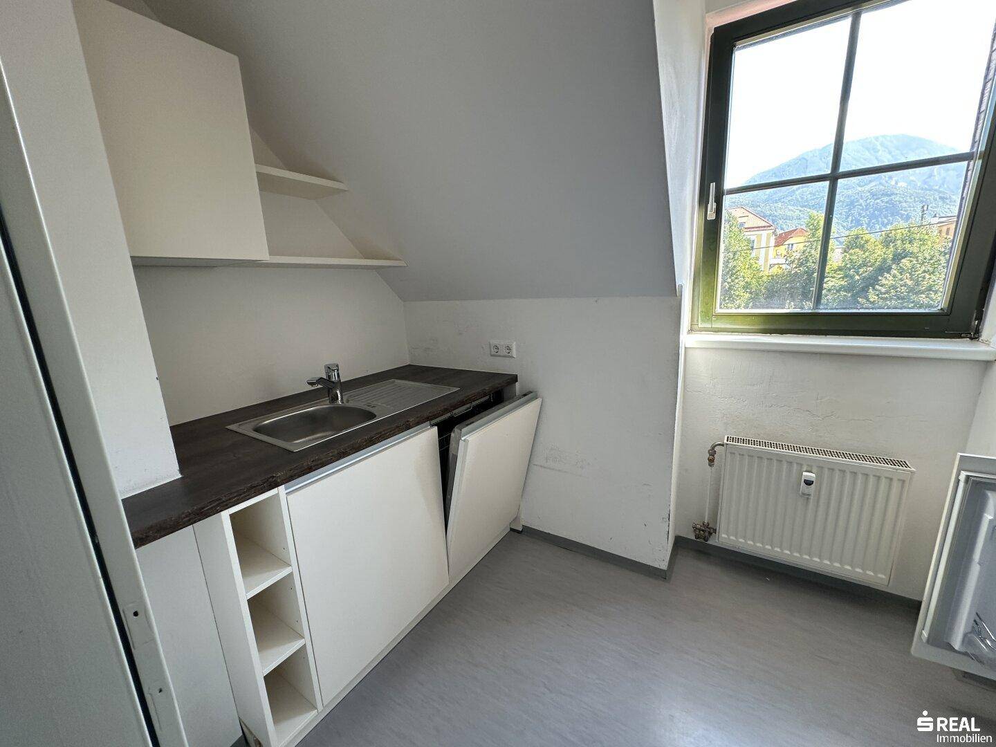 Kompakte Küchenzeile mit Spüle, Stauraum und Blick aus dem Fenster in die Berglandschaft.