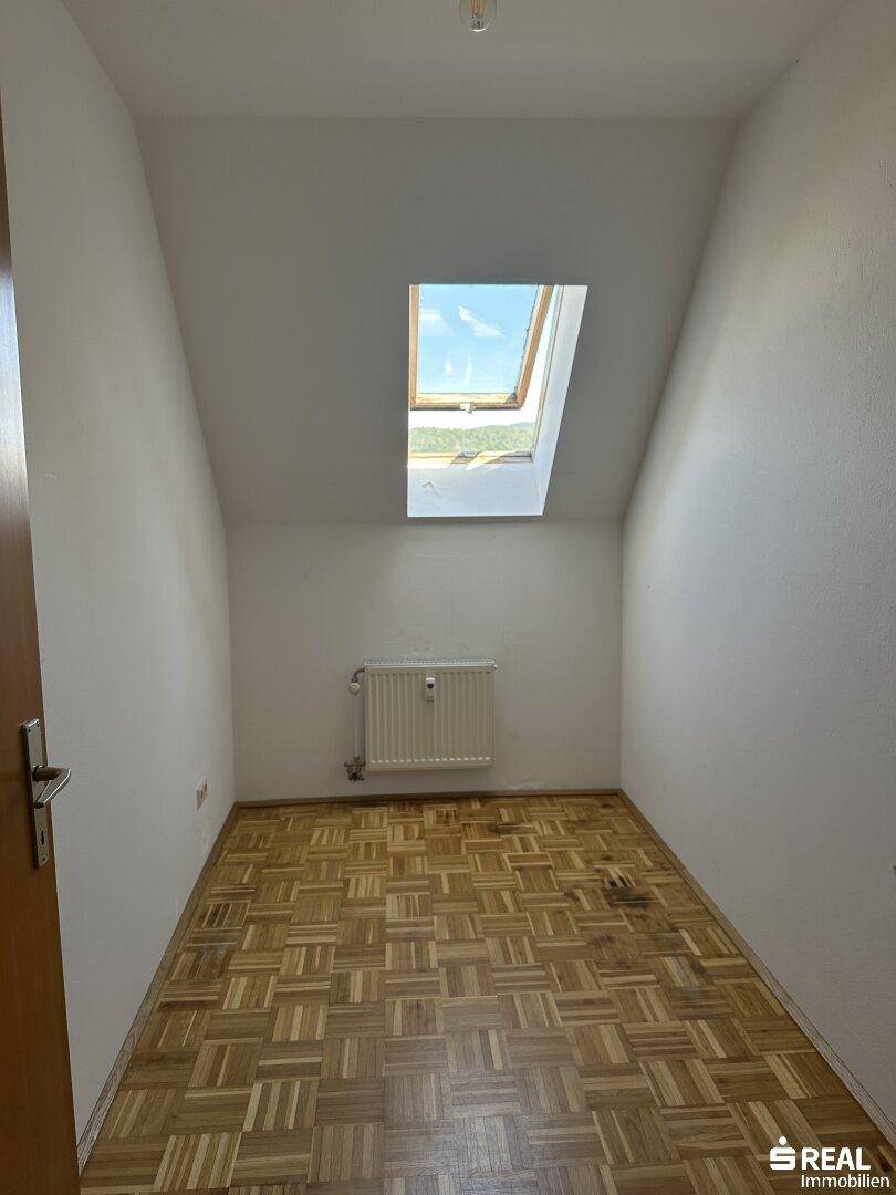 Kleines Zimmer mit Parkettboden, Dachschräge und einem Dachfenster für natürliches Licht.