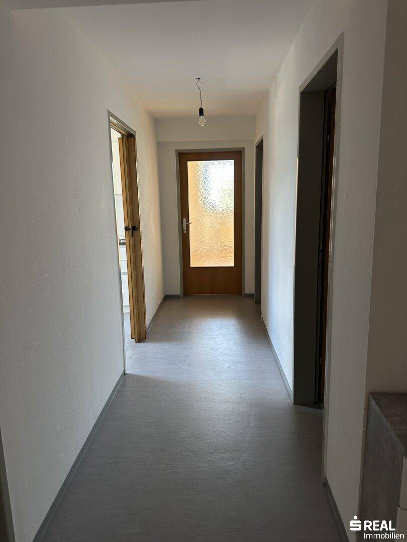 Heller Flur mit grauem Bodenbelag und Holztüren, der verschiedene Räume verbindet.