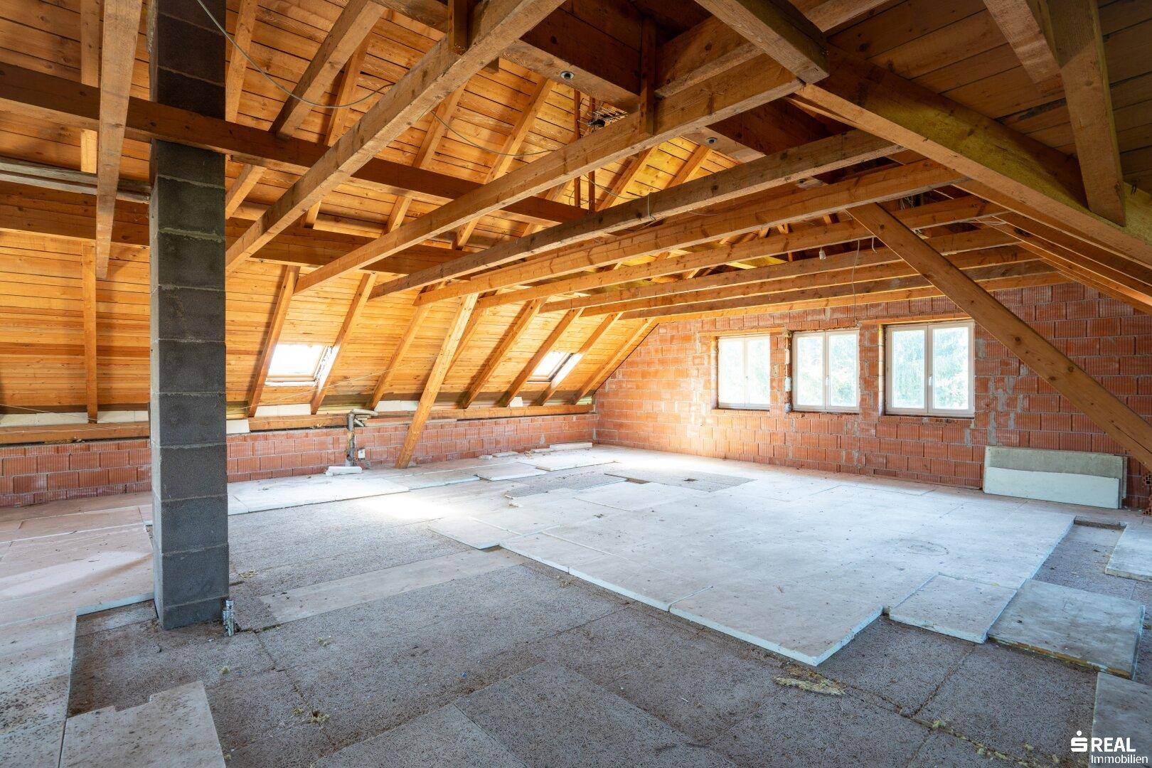 Unausgebauter Dachboden mit sichtbaren Holzbalken, Ziegelwänden und Dachfenstern, bietet Ausbaupotenzial.