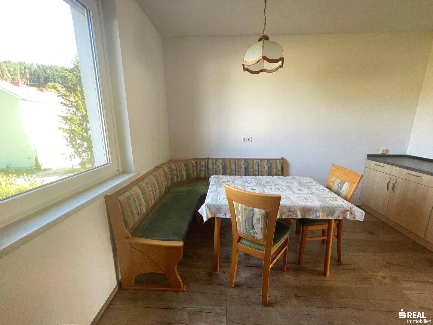 Gemütlicher Essbereich mit Eckbank, Holztisch und Blick ins Grüne durch das Fenster.