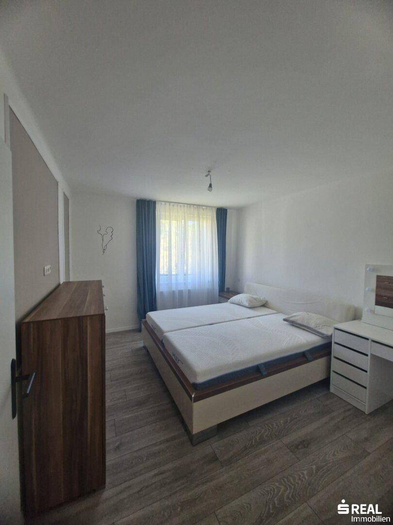 Helles Schlafzimmer mit Doppelbett, Holzkommode und Schreibtisch, ausgestattet mit Laminatboden.