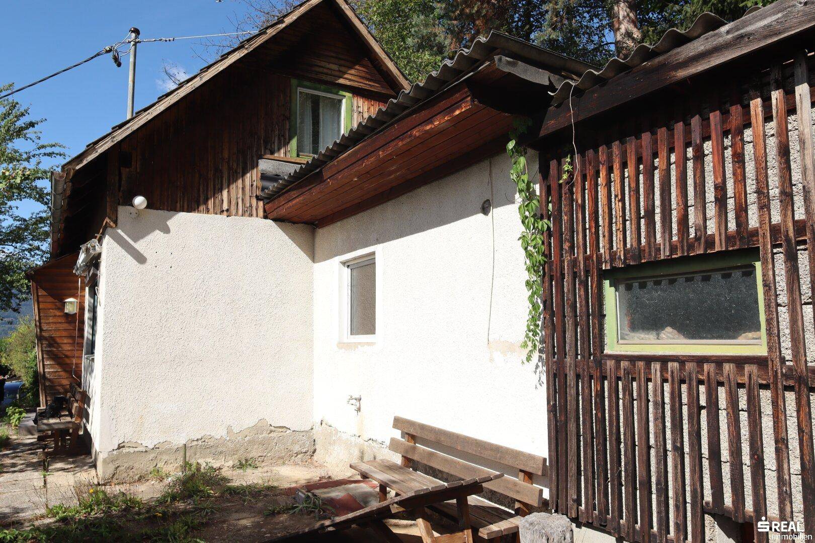 Seitenansicht des Hauses mit einer Holzbank und einer Mischung aus Putz- und Holzfassade.