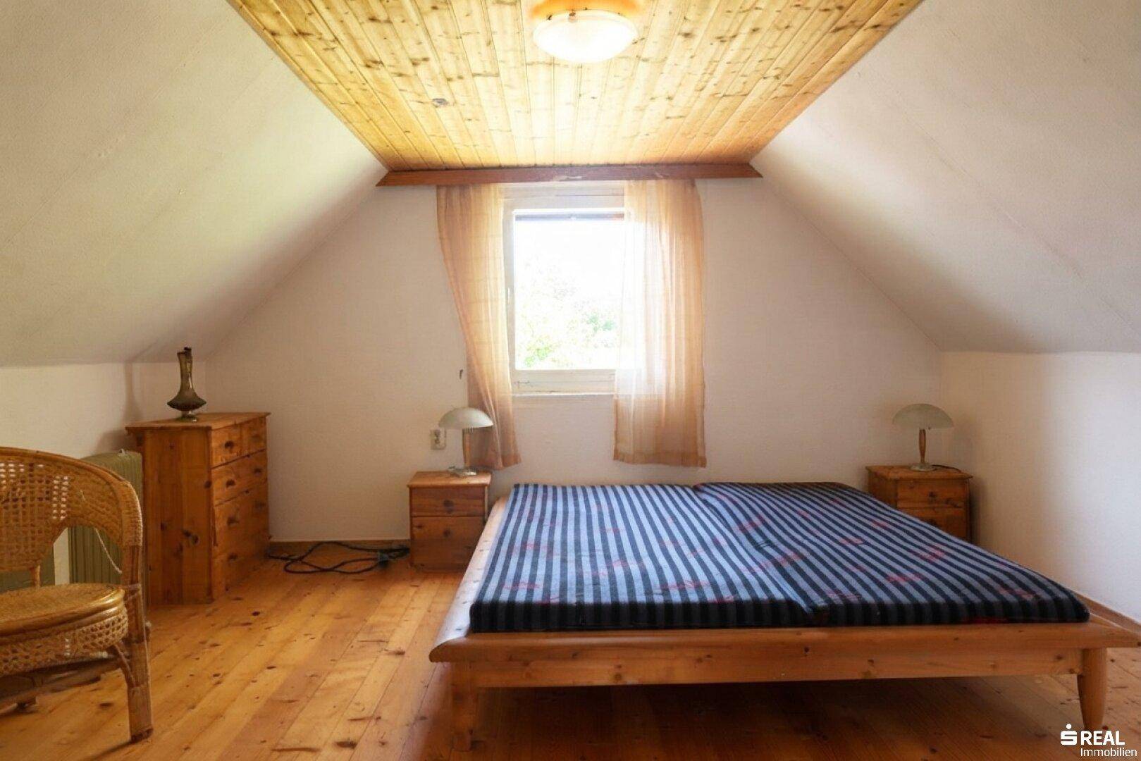 Gemütliches Schlafzimmer im Dachgeschoss mit Holzdecke, Holzboden und schrägen Wänden.