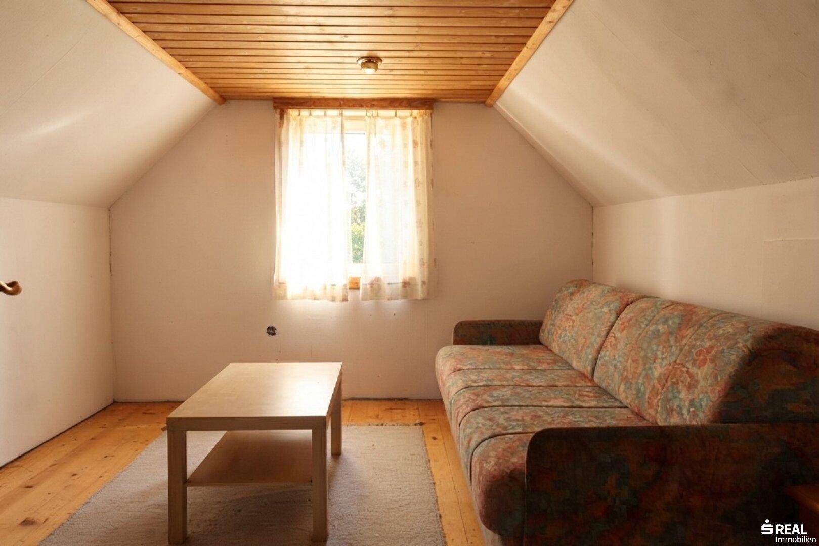 Heller Wohnraum im Dachgeschoss mit Holzboden, Holzdecke und schrägen Wänden, ideal als Gästezimmer.