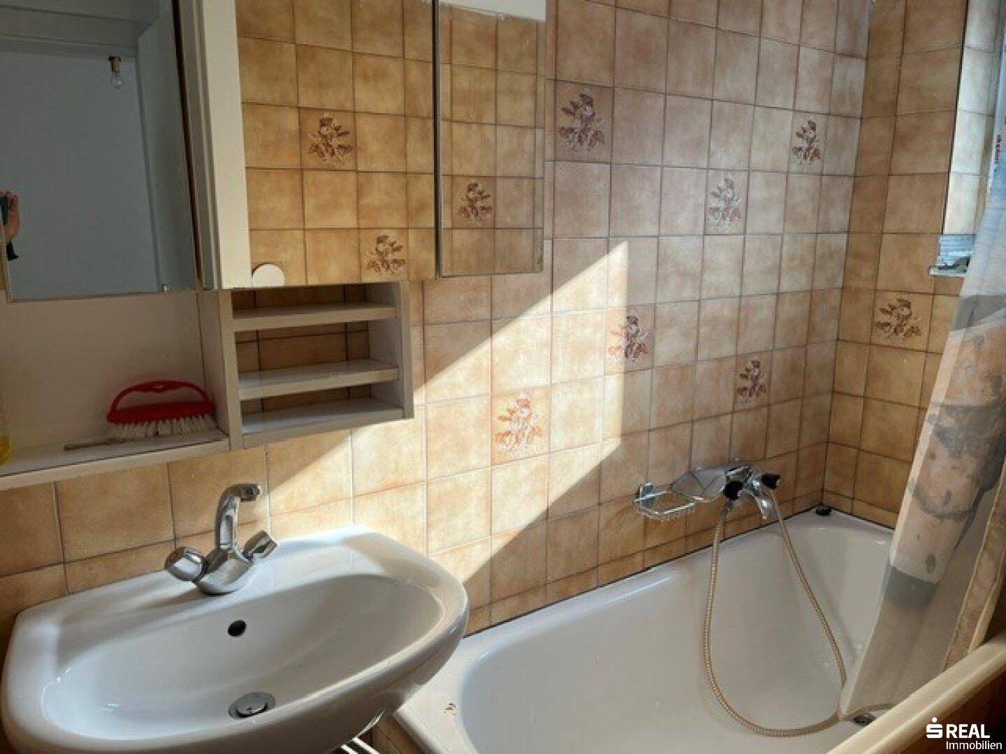 Badezimmer im älteren Stil mit Badewanne, Waschbecken und gemusterten beigen Fliesen.