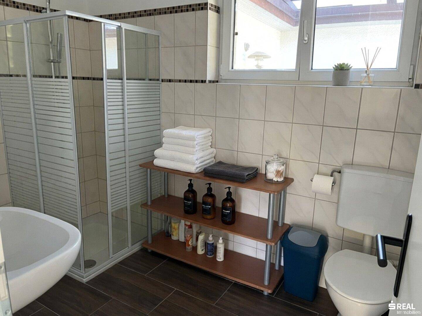 Modernes Badezimmer mit Duschkabine, WC und Fenster, ausgestattet mit dunklen Bodenfliesen.