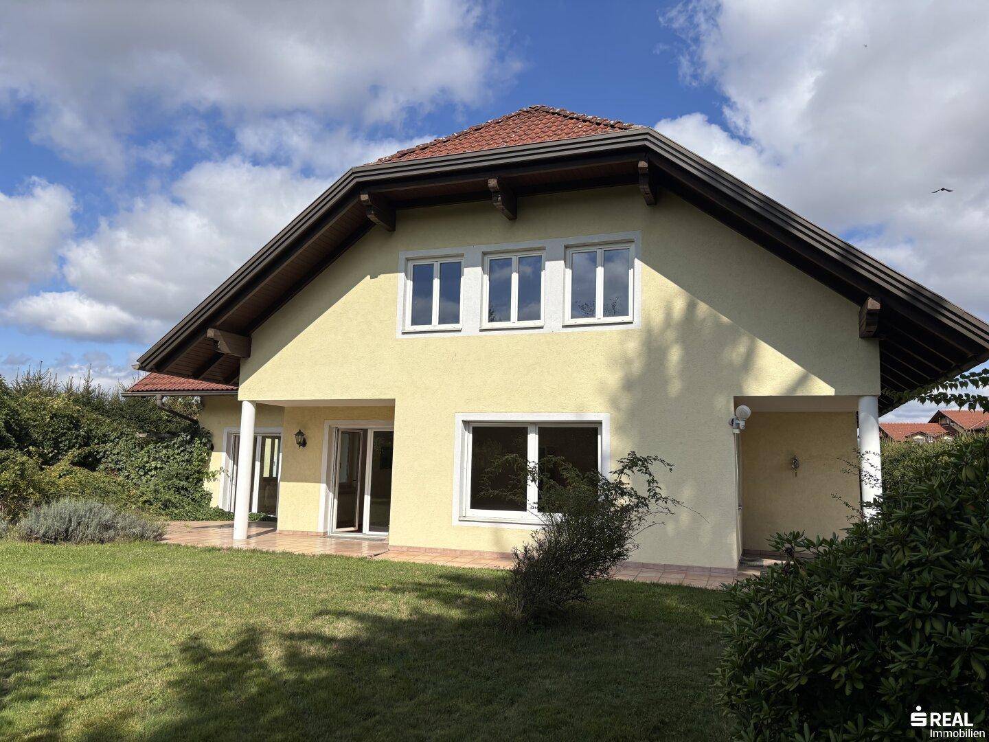 Ansicht des Hauses mit gelber Fassade, großen Fenstern und grünem Vorgarten.