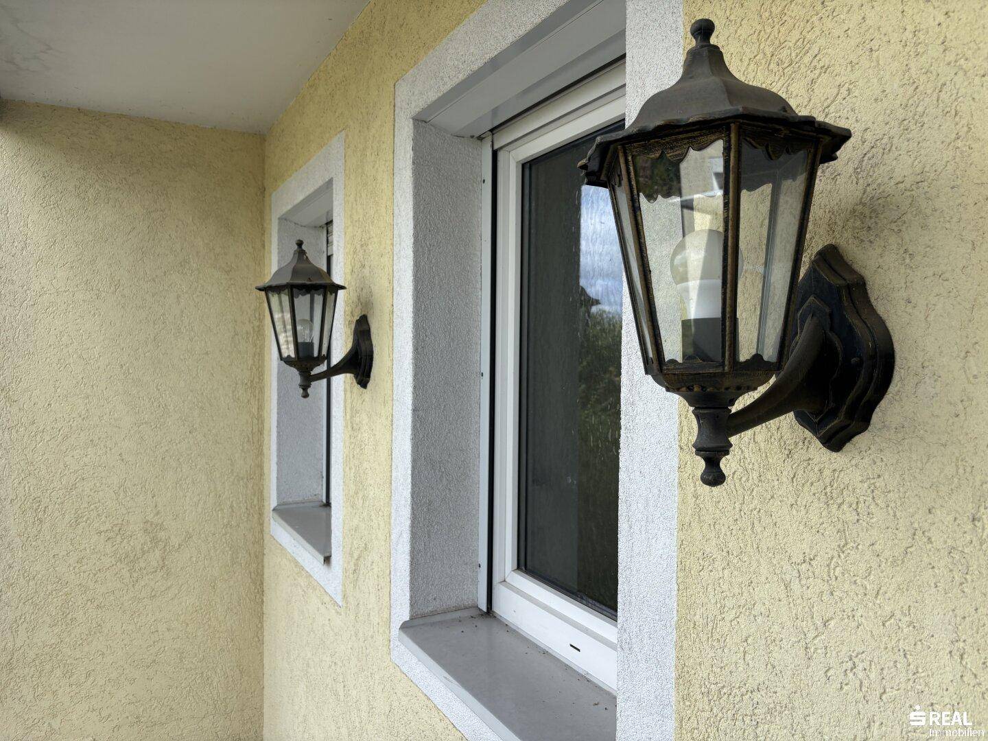 Detailansicht einer klassischen Außenleuchte neben einem Fenster an der gelben Fassade.