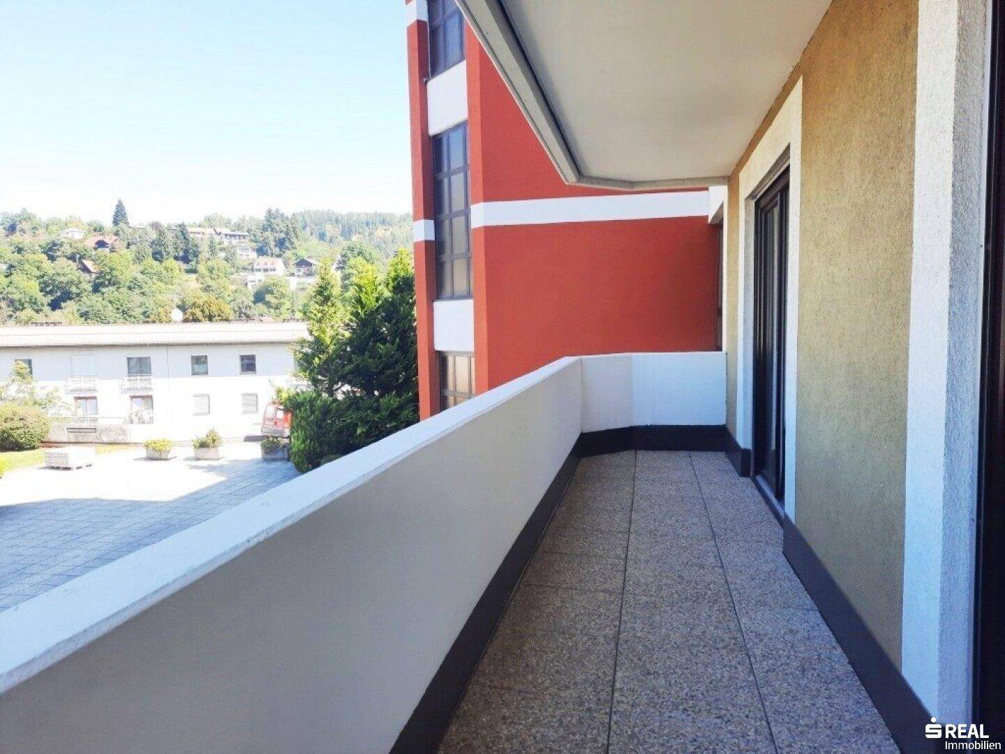 Geräumiger Balkon mit Fliesenboden und Blick auf die umliegende Wohngegend und grüne Hügel.