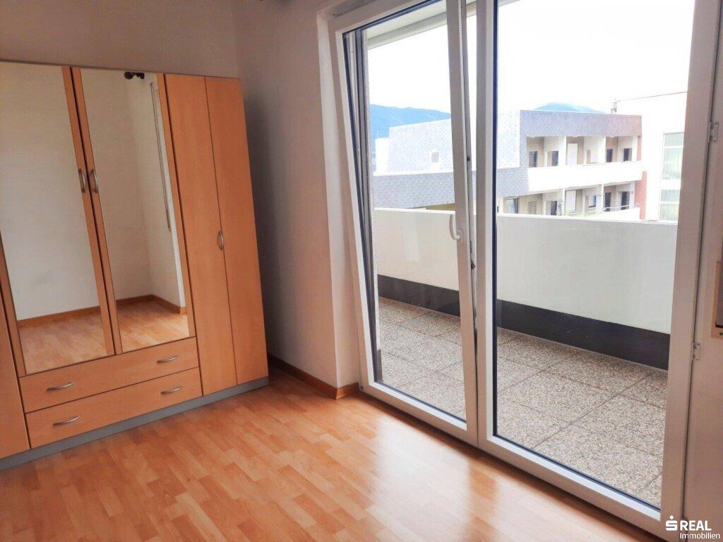Schlafzimmer mit Laminatboden, Spiegelschrank und großem Schiebetürzugang zum Balkon.