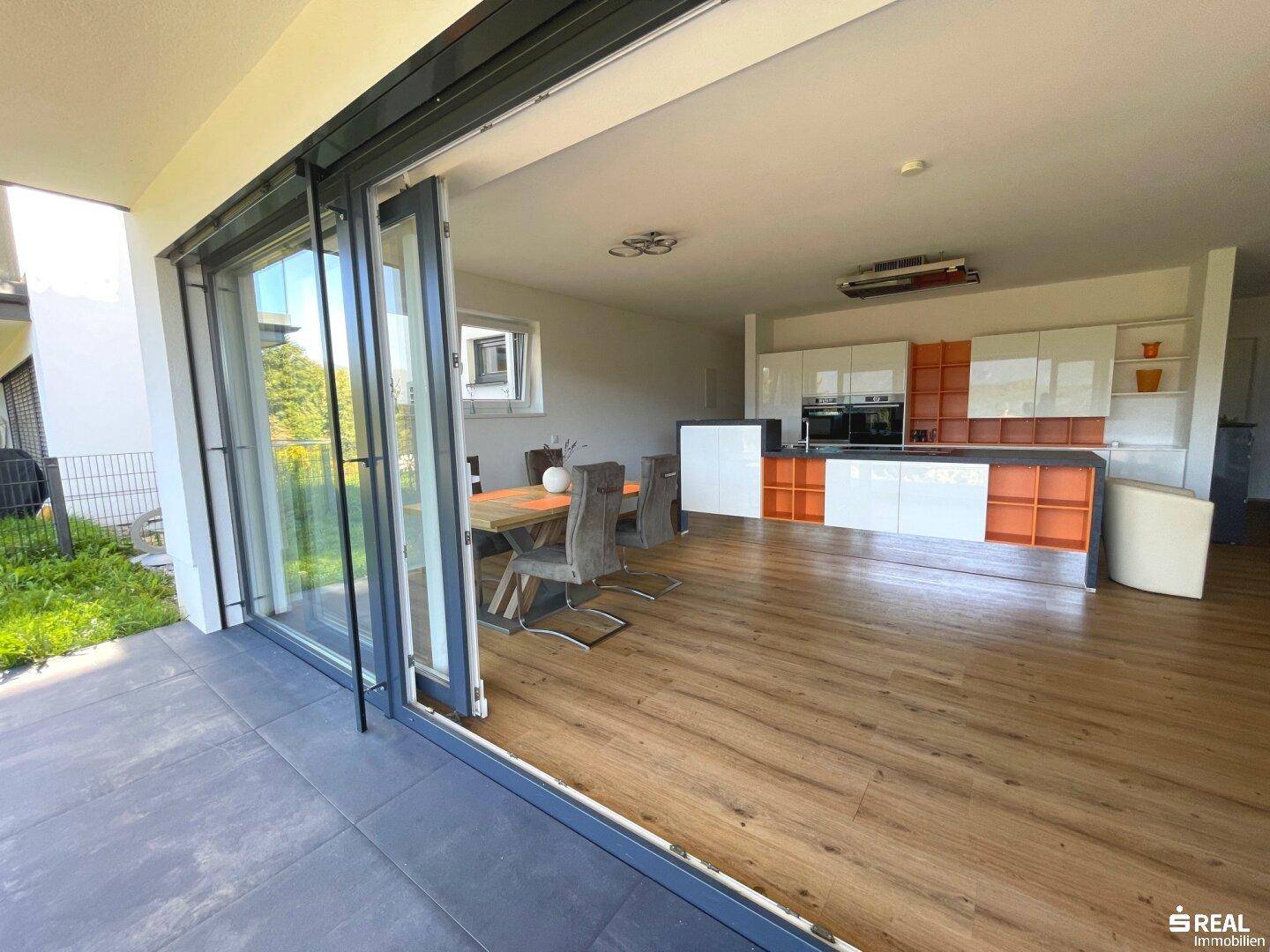 Heller offener Wohnbereich mit moderner Küche, Holzboden und Zugang zur Terrasse.