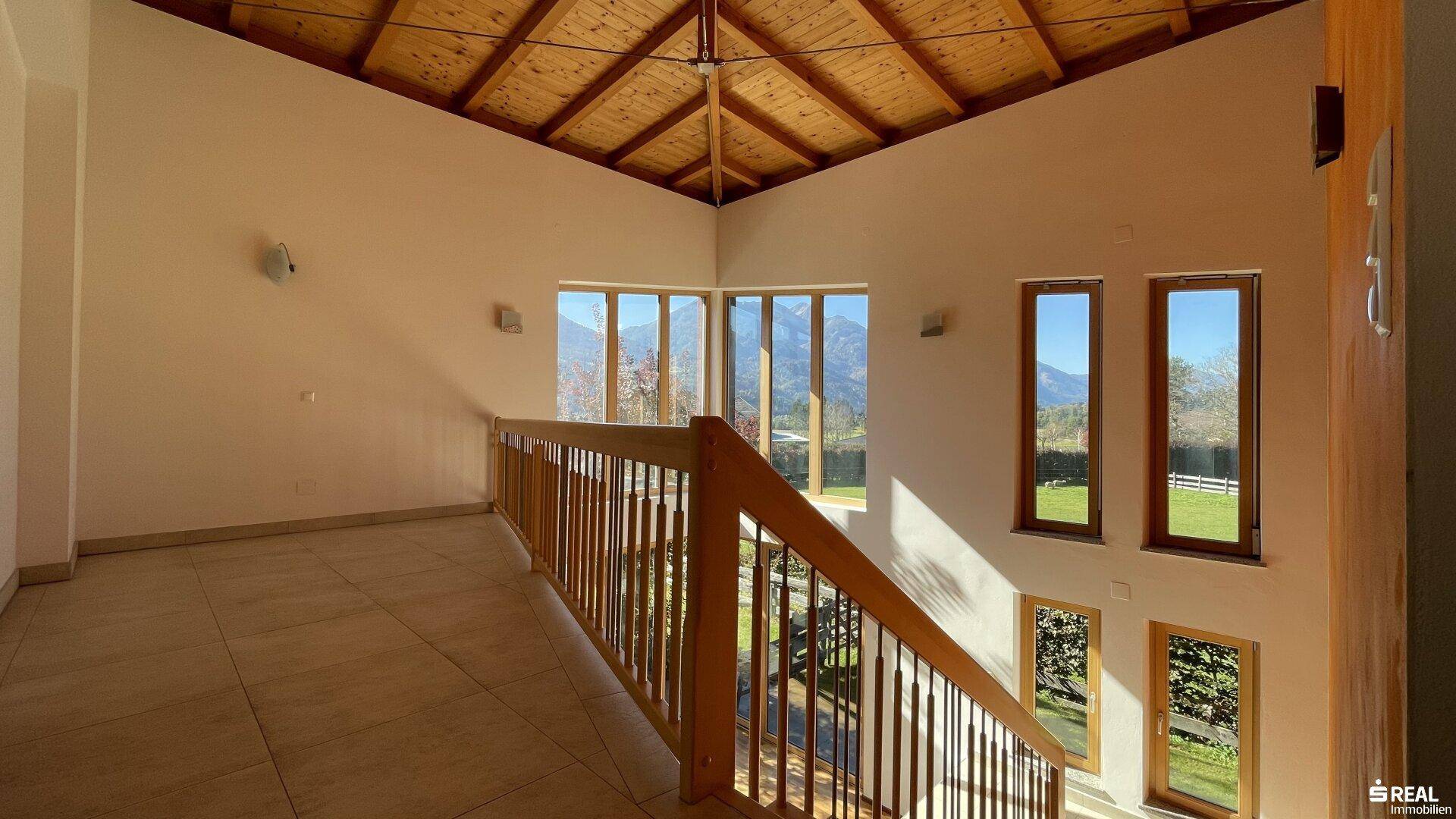 Heller Flur im Obergeschoss mit Holzgeländer, Holzdach und Bergblick durch die Fenster.