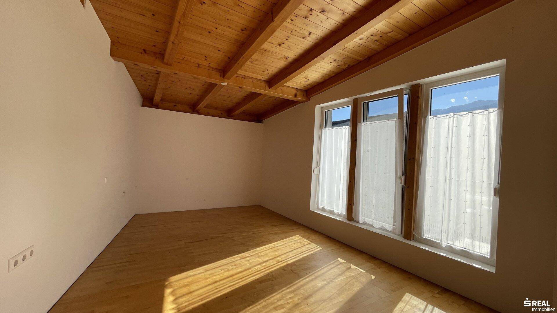 Helles Schlafzimmer mit Holzbalkendecke und großen Fenstern, die viel Licht hereinlassen.