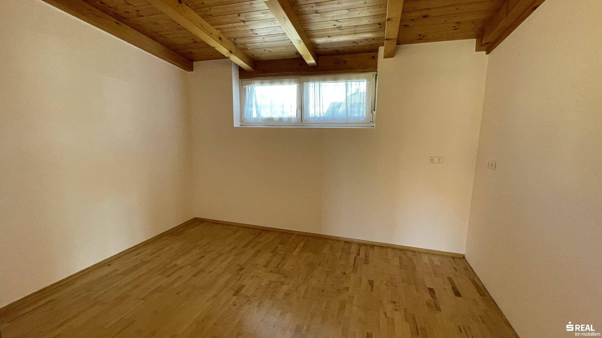 Ruhiges Schlafzimmer mit Holzboden, Holzbalkendecke und einem Fenster.